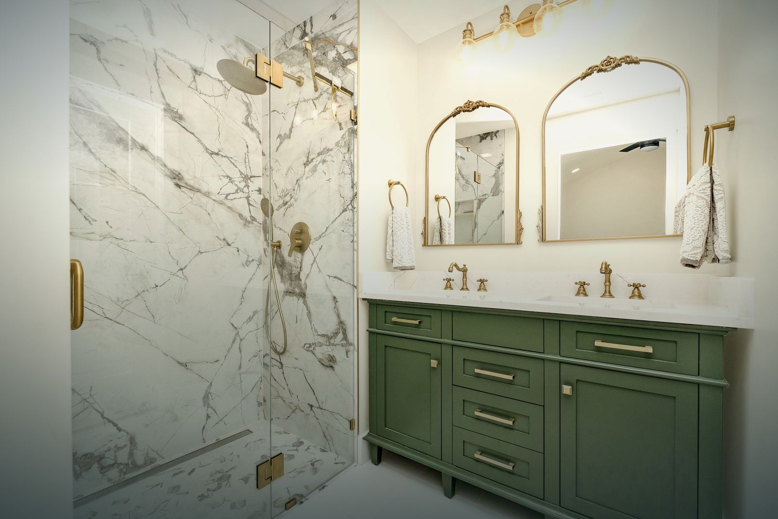 Renovated bathroom with a marble walk-in shower, green double vanity and brass fixtures