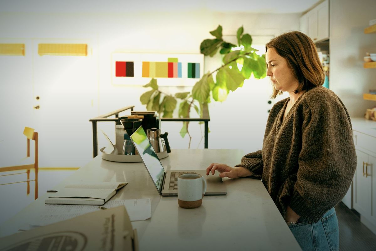 Self-employed woman reviewing her business accounts on a laptop at her kitchen counter
